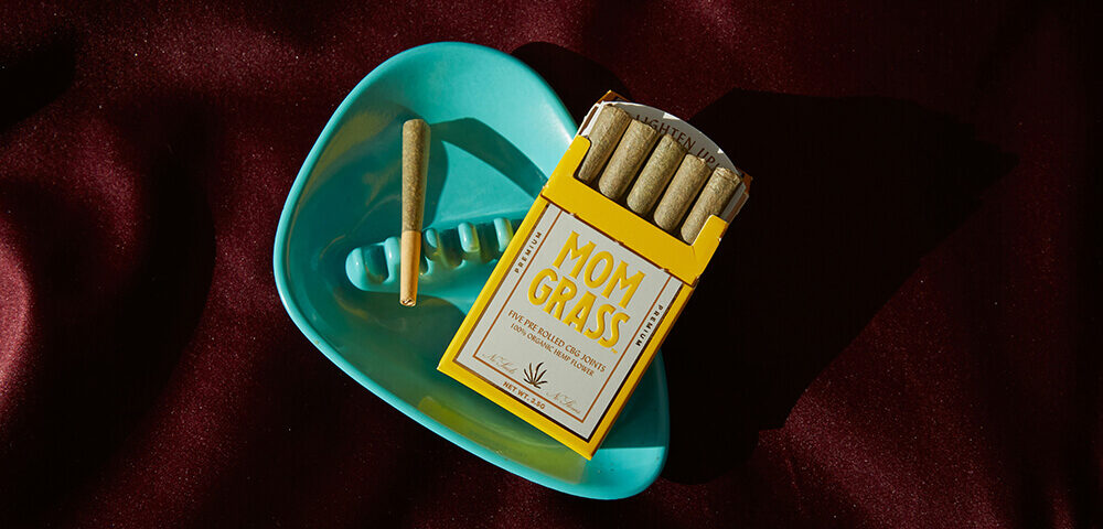 weed packaging ideas: custom pre-roll packaging featuring a "Mom Grass" brand box with rolled joints and a turquoise ashtray