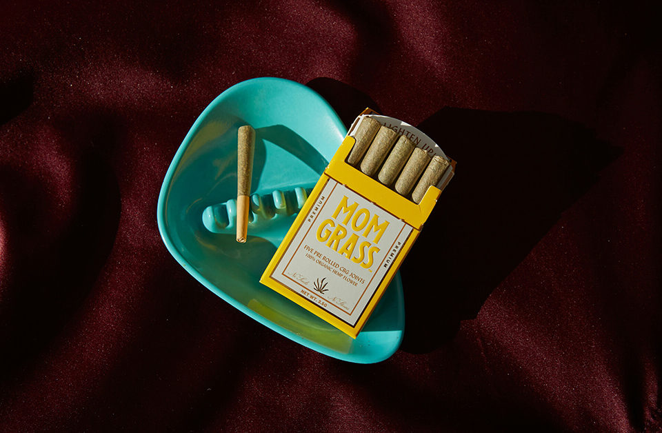 weed packaging ideas: custom pre-roll packaging featuring a "Mom Grass" brand box with rolled joints and a turquoise ashtray