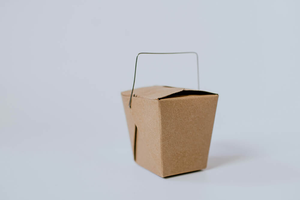 A small, custom kraft takeout box with a metal handle, ideal for packaging cannabis edibles or small items.