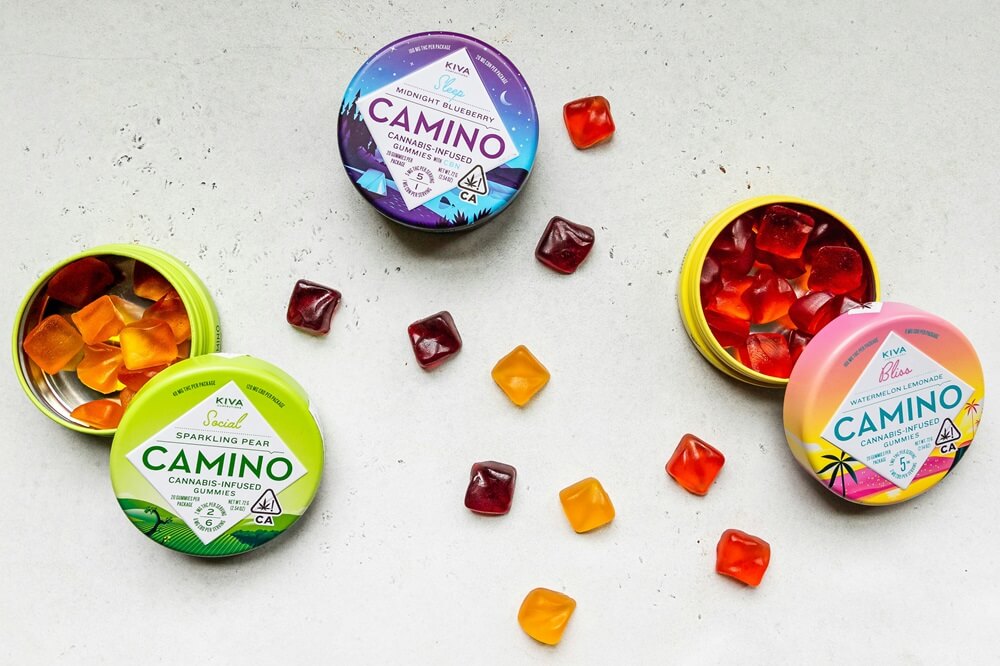 Kiva Camino cannabis-infused gummies in colorful tins with scattered pieces