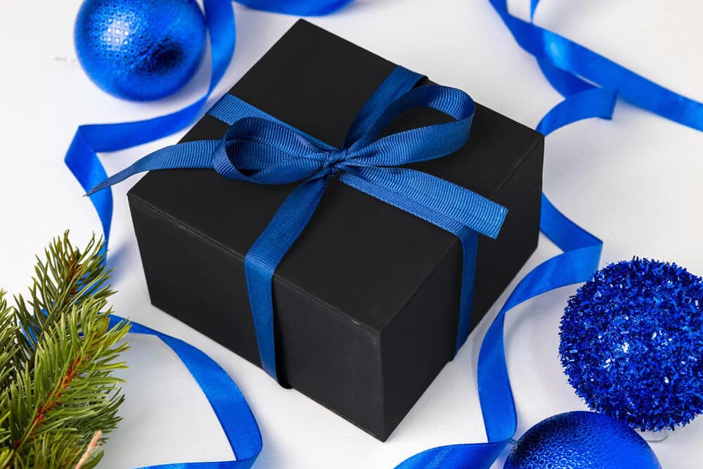 Black gift box with ribbon surrounded by festive blue decorations