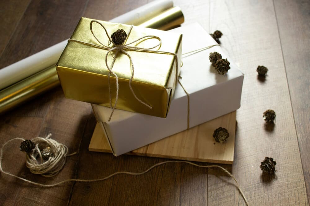 Holiday-themed gold and white gift boxes with ribbon and pine accents