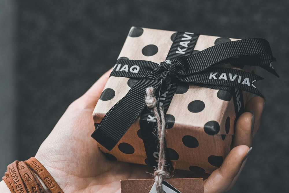 Hand holding a polka dot gift box with branded ribbon for cannabis product