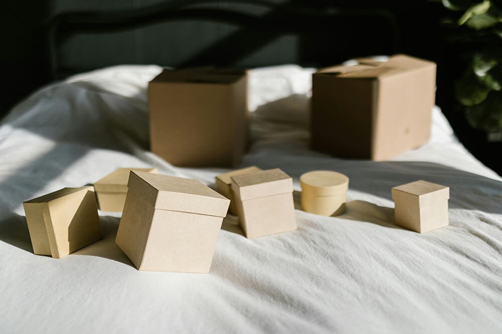 A variety of small and large kraft paper gift boxes displayed on a bed