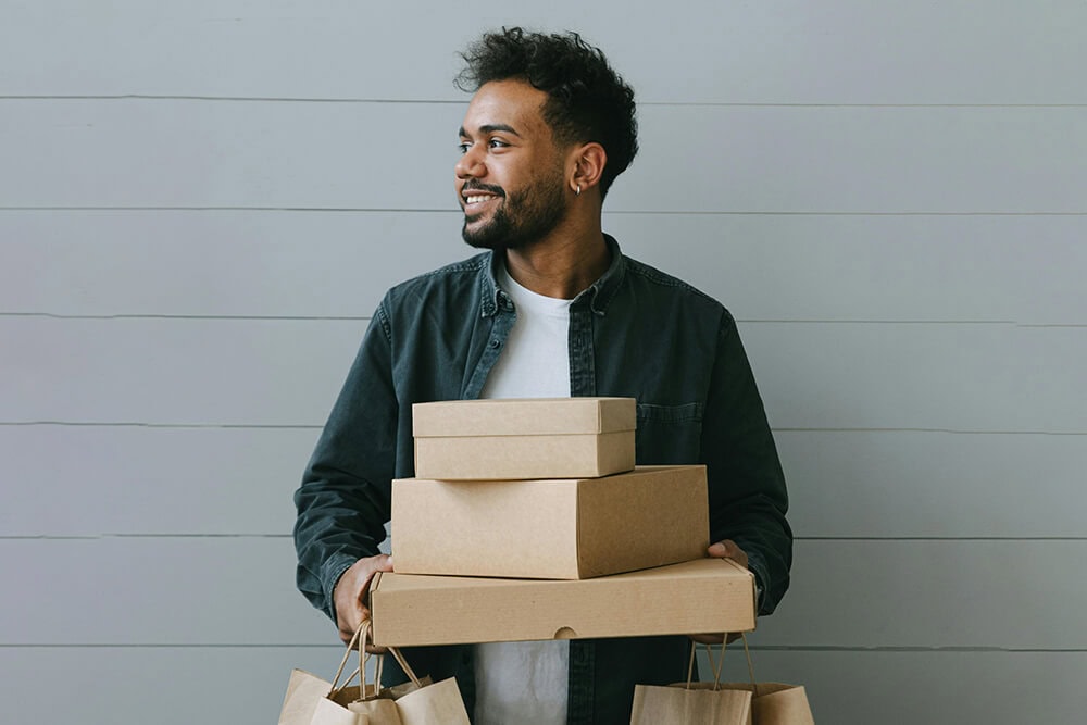 Man holding several kraft cardboard boxes and shopping bags with a smile