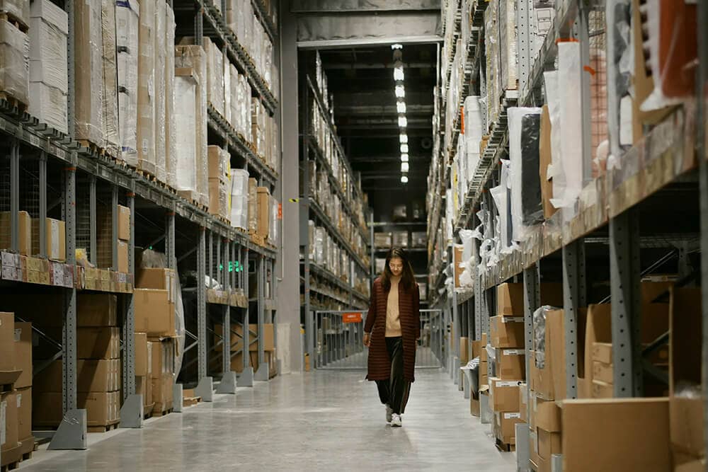A person walking through a well-organized warehouse aisle full of packaged goods.