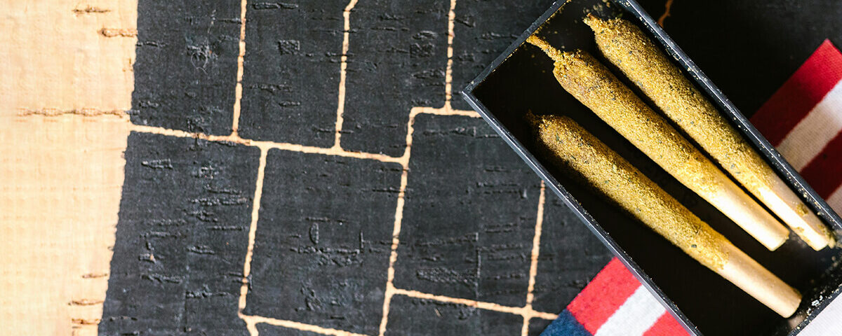 Close-up of three kief-coated pre rolled blunts in a black tray on an American flag background