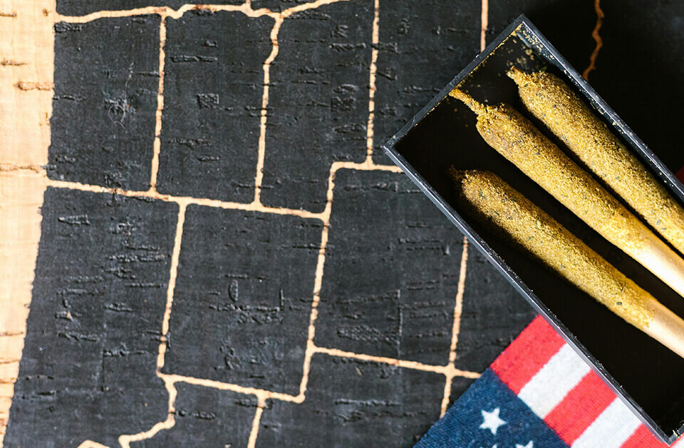 Close-up of three kief-coated pre rolled blunts in a black tray on an American flag background