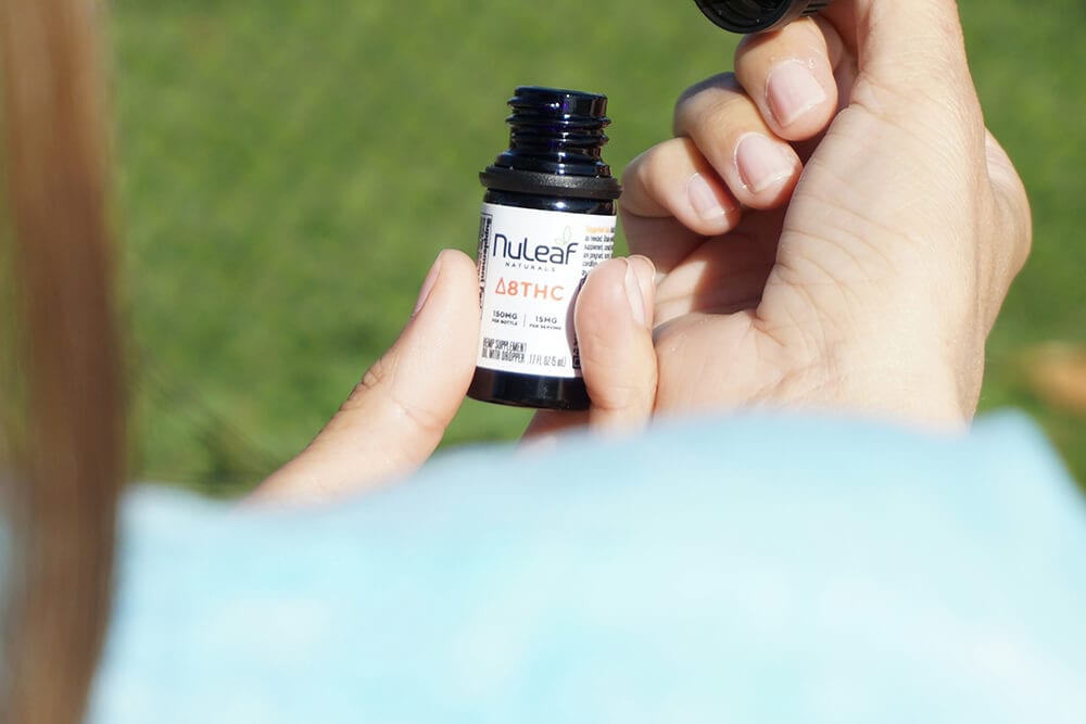 Close-up of Delta 8 THC tincture bottle held in hand outdoors