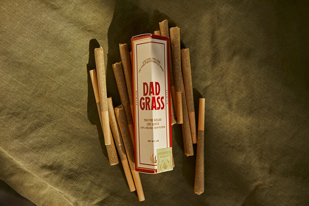 Retro-style Dad Grass pre-roll packaging with cannabis joints on fabric background