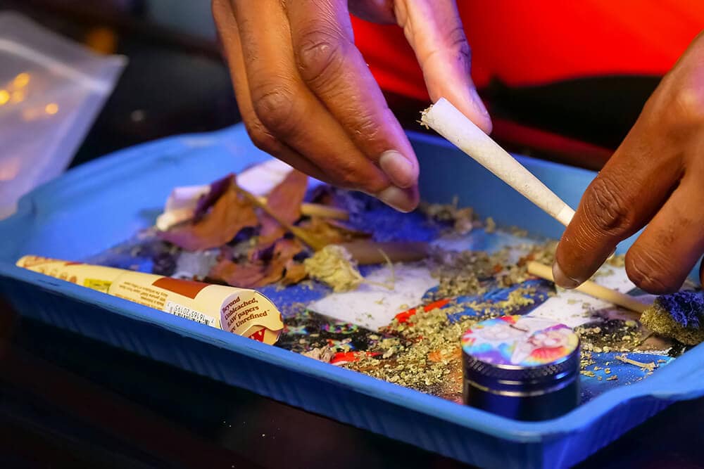 Person rolling a blunt on a blue weed rolling tray filled with cannabis material.