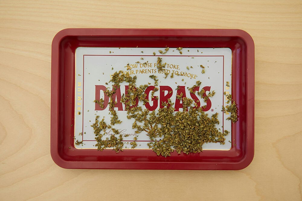 Red metal weed rolling tray with cannabis scattered on it, branded with “Dad Grass”.