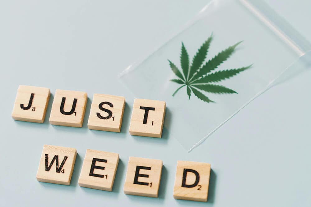 Weed leaf sticker on bag next to scrabble tiles spelling “JUST WEED.”