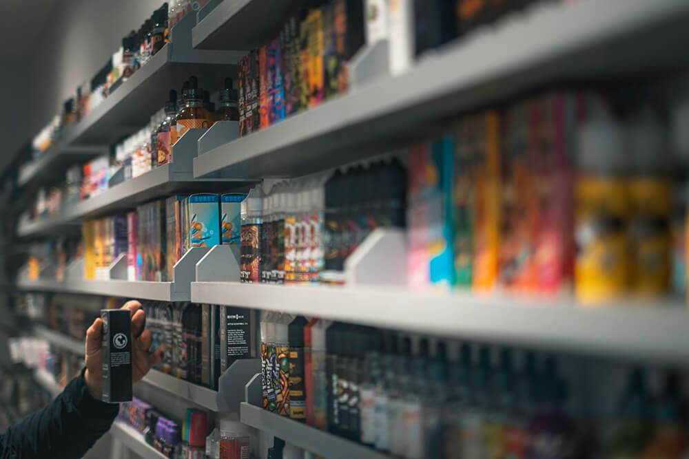 Vape shop shelf displaying a wide variety of e-liquid and disposable vape products