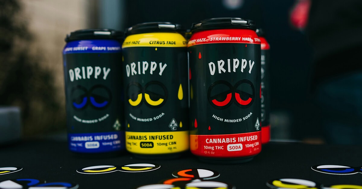 Three cans of Drippy cannabis beverage soda in grape, citrus, and strawberry flavors.