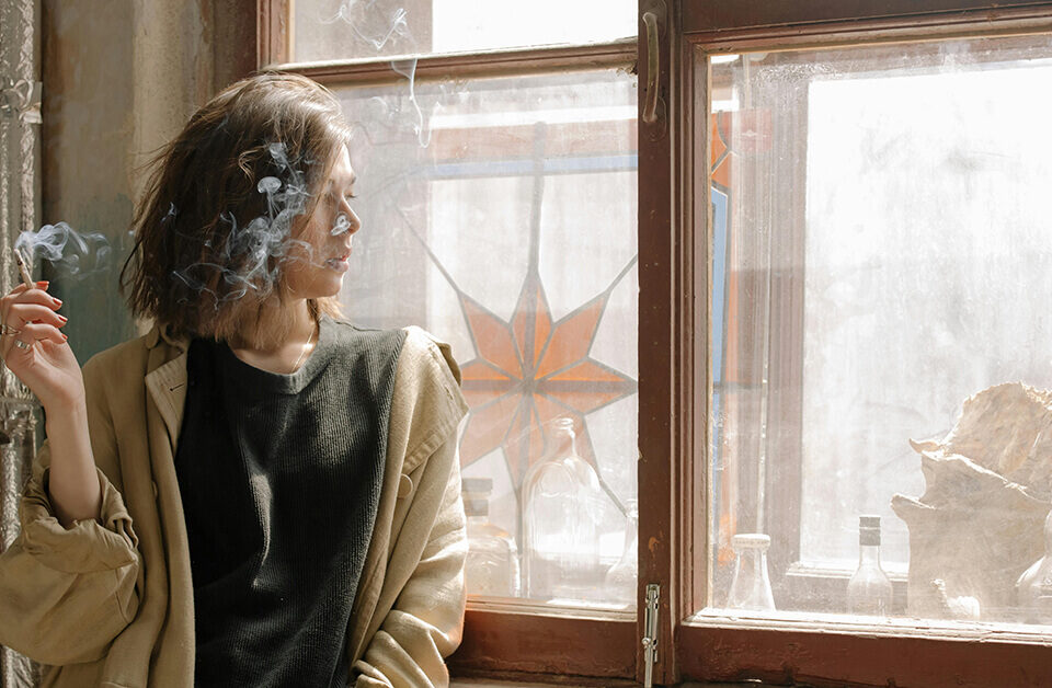 Woman enjoying a mini blunt by the window with sunlight streaming in.