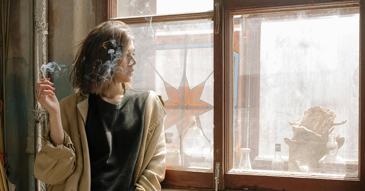 Woman enjoying a mini blunt by the window with sunlight streaming in.