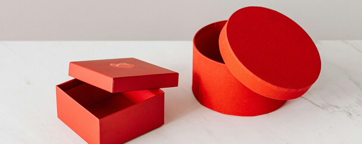 A red square gift box with lid and a round red gift box with lid, both displayed on a marble surface.