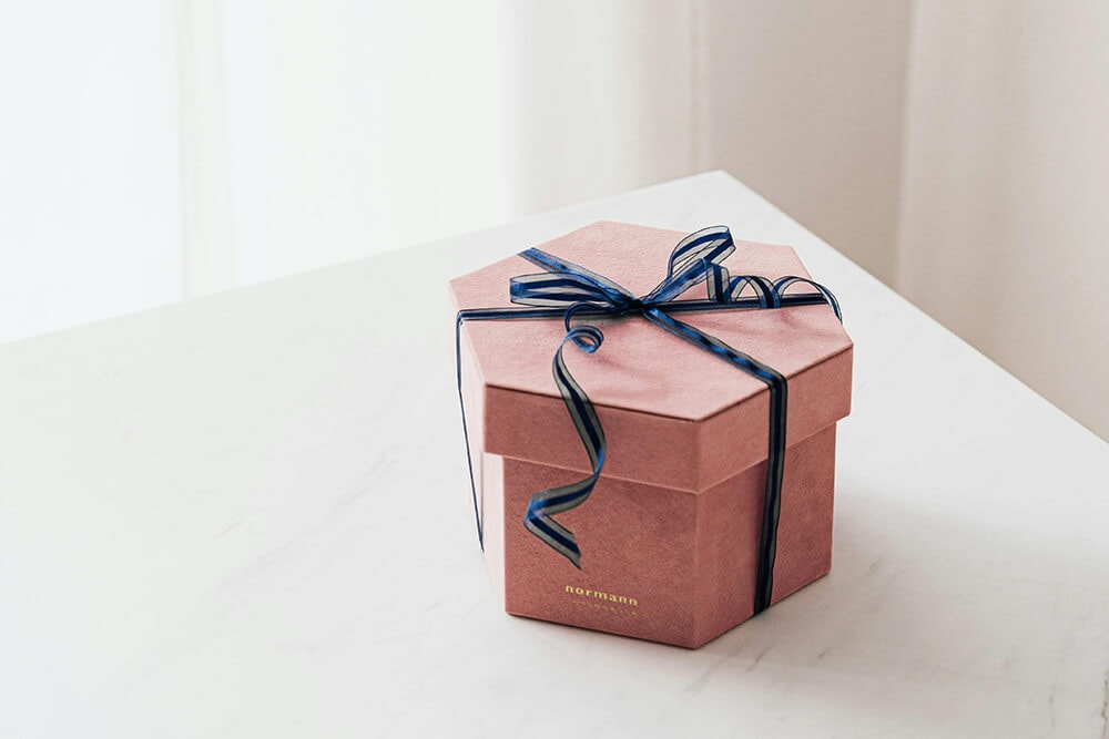 A hexagonal pink gift box with lid, tied with a navy ribbon, showcasing a stylish and modern design for gifting.