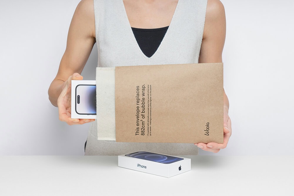 Person inserting an iPhone box into a protective kraft padded mailer