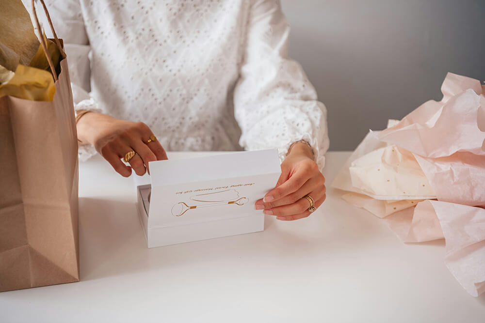 Hands unboxing jewelry from a white luxury rigid box with premium gold detailing.