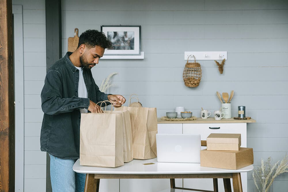 Man preparing paper bags and boxes for e-commerce orders in a cozy home office setup.