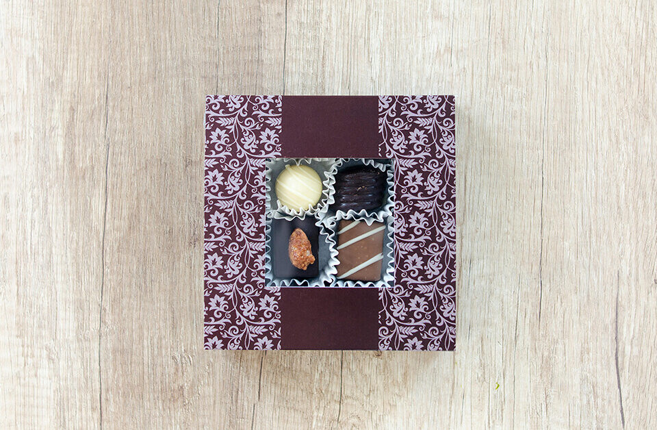 Top view of custom chocolate gift boxes with a floral pattern and a clear square window showing four truffles.