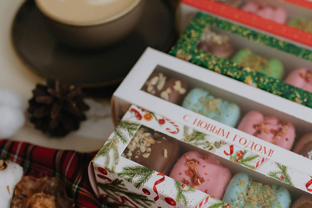 Festive custom printed chocolate boxes with holiday graphics and rectangular windows showing colorful treats.