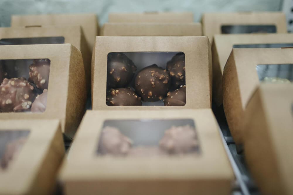 Rows of eco-friendly kraft paper custom chocolate boxes with windows displaying chocolate clusters.