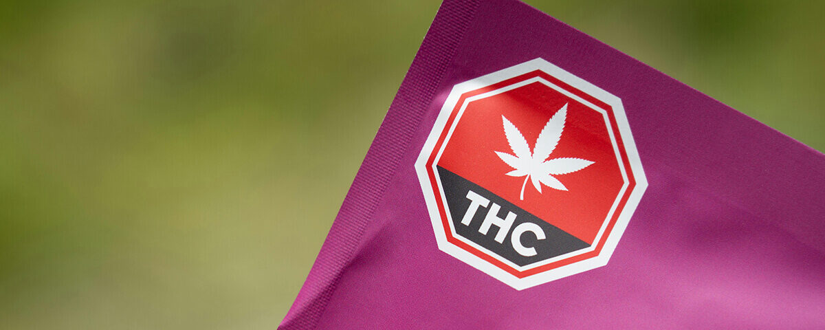 Close-up of purple marijuana packaging bags featuring a mandated red and black universal THC warning symbol.