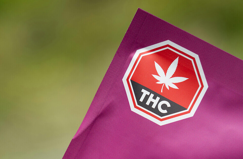 Close-up of purple marijuana packaging bags featuring a mandated red and black universal THC warning symbol.