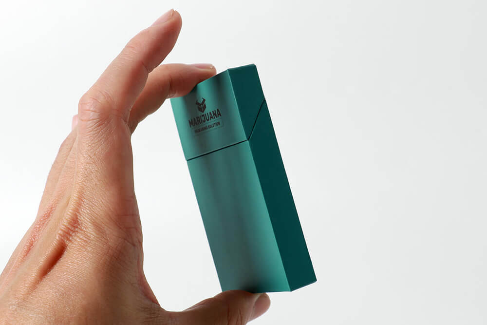 A detailed profile photograph of the custom-branded teal paper carton, held between fingertips, emphasizing its slim profile and rigid structural integrity required for discreet vape packaging.